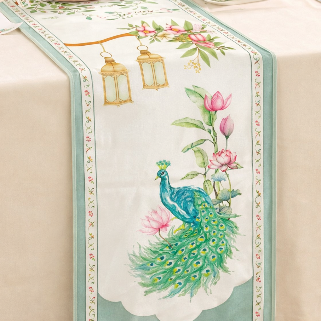Cream table runner with a green peacock and pink flowers inside a green border.