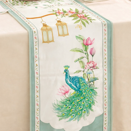Cream table runner with a green peacock and pink flowers inside a green border.