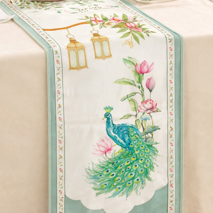 Cream table runner with a green peacock and pink flowers inside a green border.