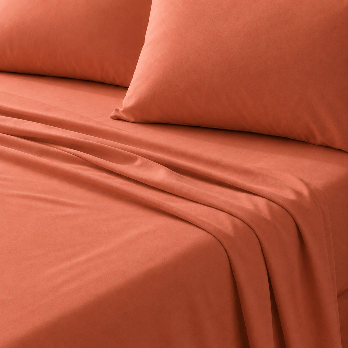 Close-up of a burnt orange bedsheet and matching pillow on a bed.
