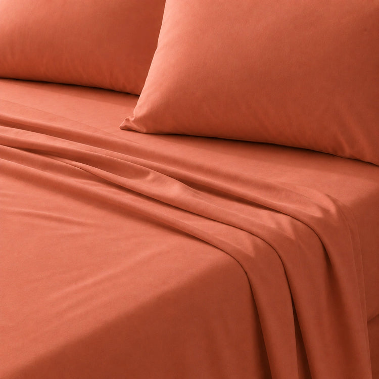 Close-up of a burnt orange bedsheet and matching pillow on a bed.