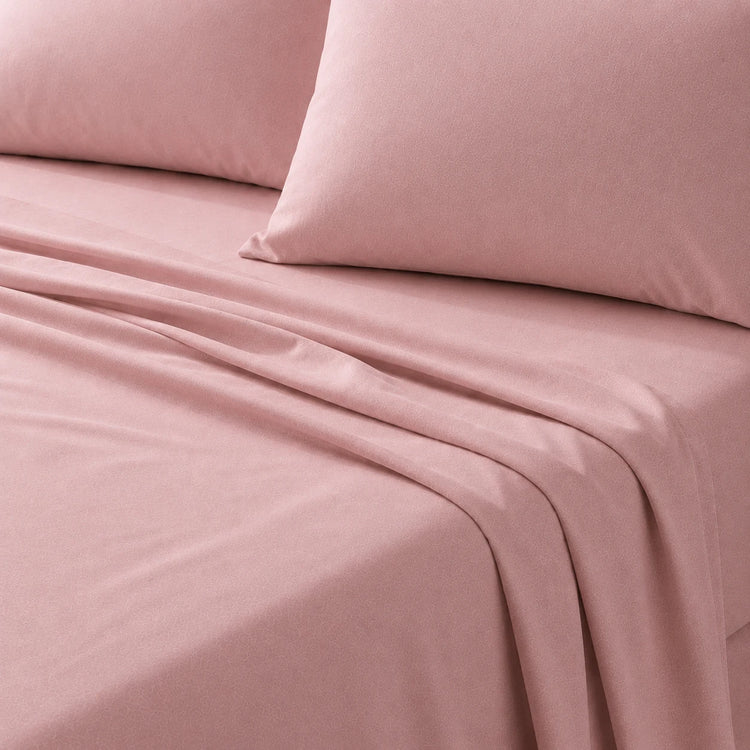 Close-up of a dusty rose bedsheet and matching pillow on a bed.