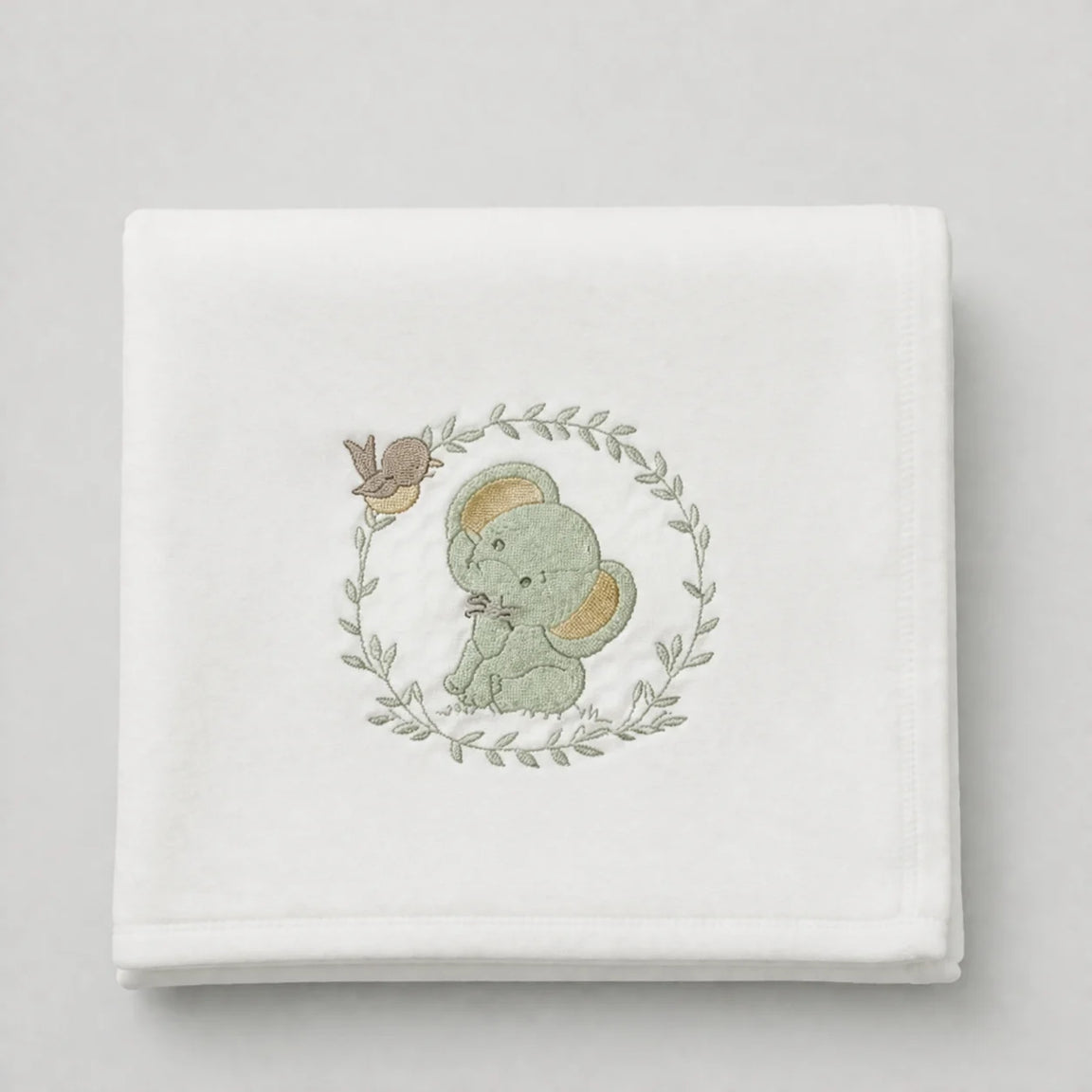 White blanket folded flat with a pale green elephant and leafy wreath motif