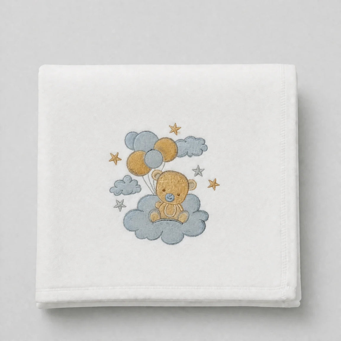 White blanket folded flat with a teddy bear holding balloons among clouds and stars