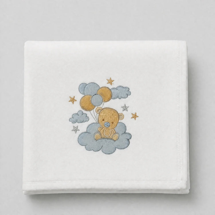 White blanket folded flat with a teddy bear holding balloons among clouds and stars