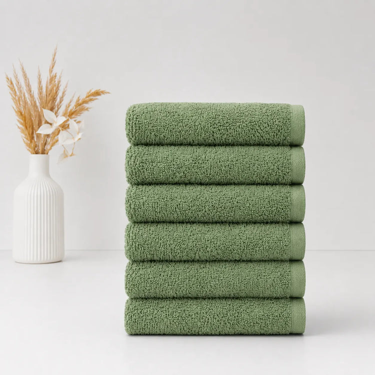 Stack of six sage green hand towels beside a white vase.