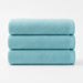 Three folded turquoise cotton bath towels stacked together.