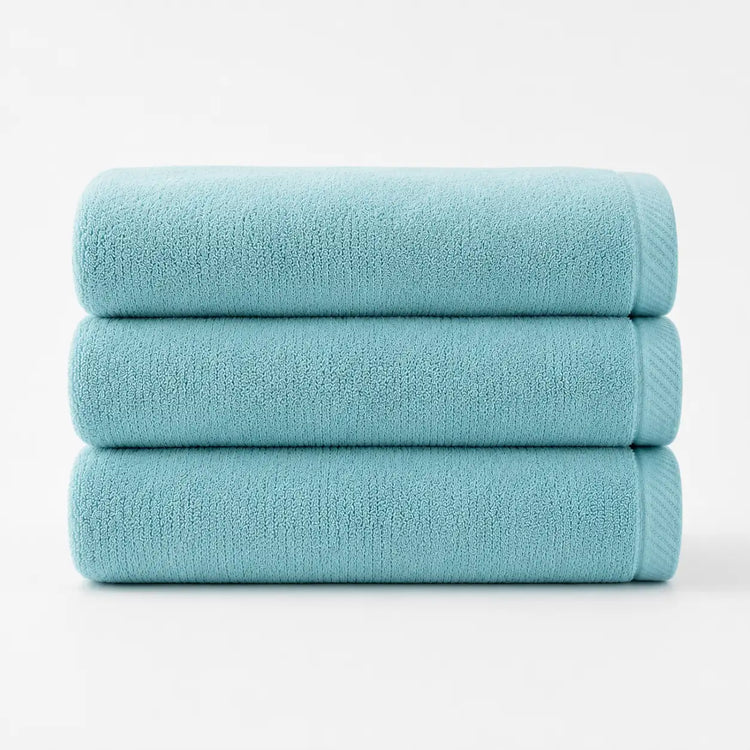 Three folded turquoise cotton bath towels stacked together.