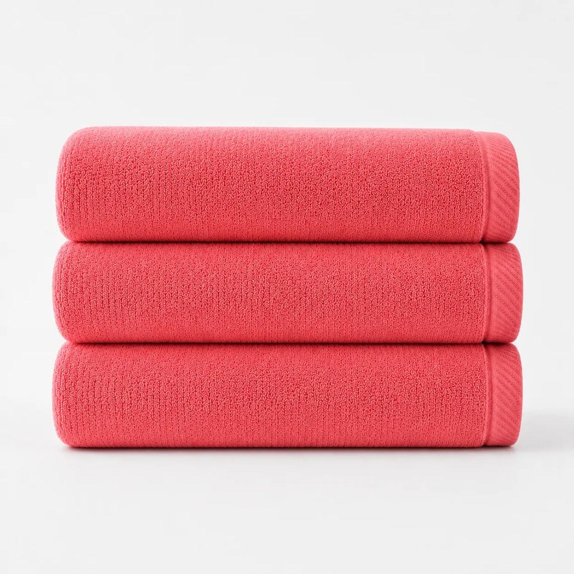 Three folded coral cotton bath towels stacked together.