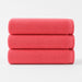 Three folded coral cotton bath towels stacked together.