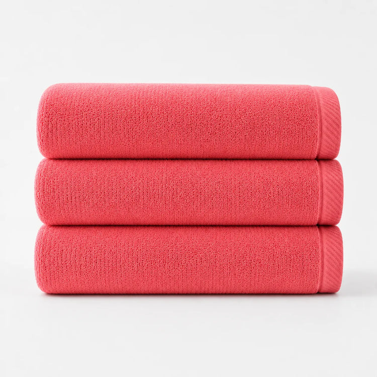 Three folded coral cotton bath towels stacked together.