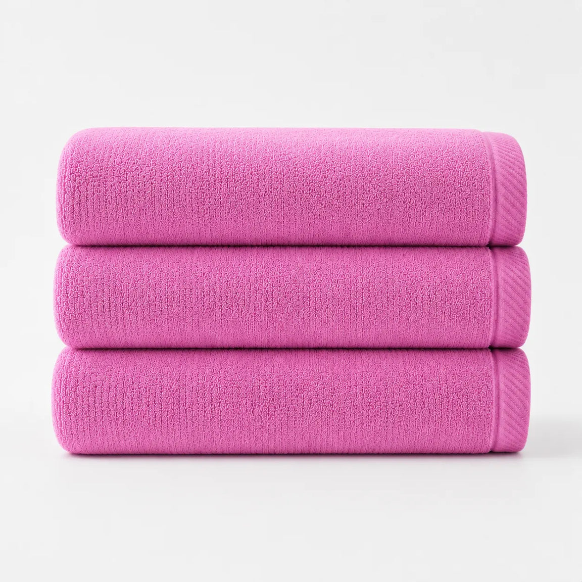 Three folded bright pink cotton bath towels stacked together.