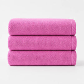 Three folded bright pink cotton bath towels stacked together.