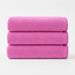 Three folded bright pink cotton bath towels stacked together.