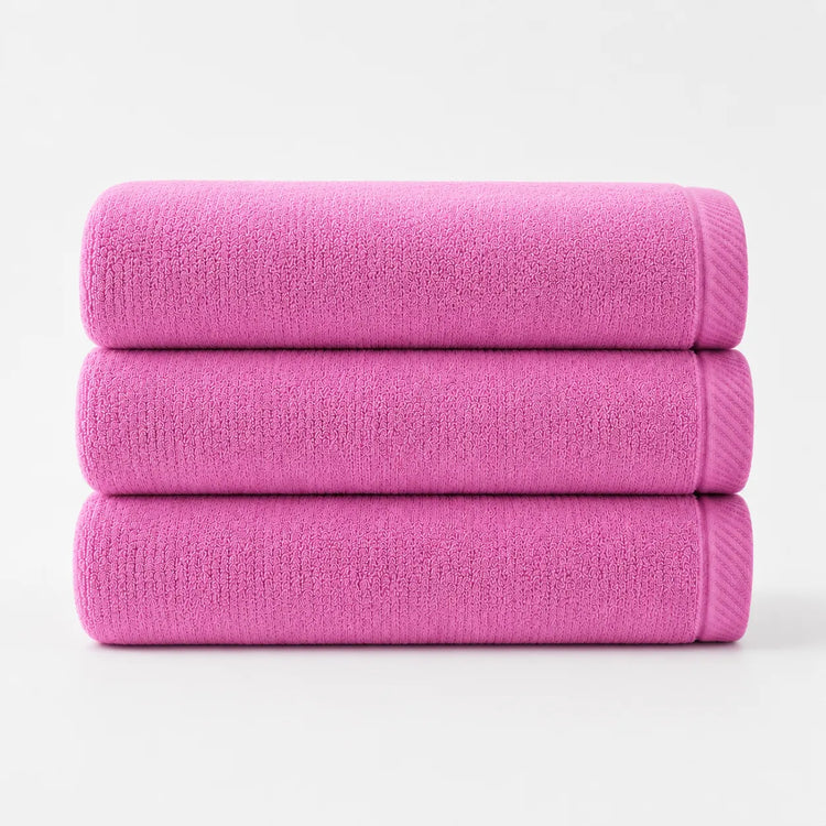 Three folded bright pink cotton bath towels stacked together.