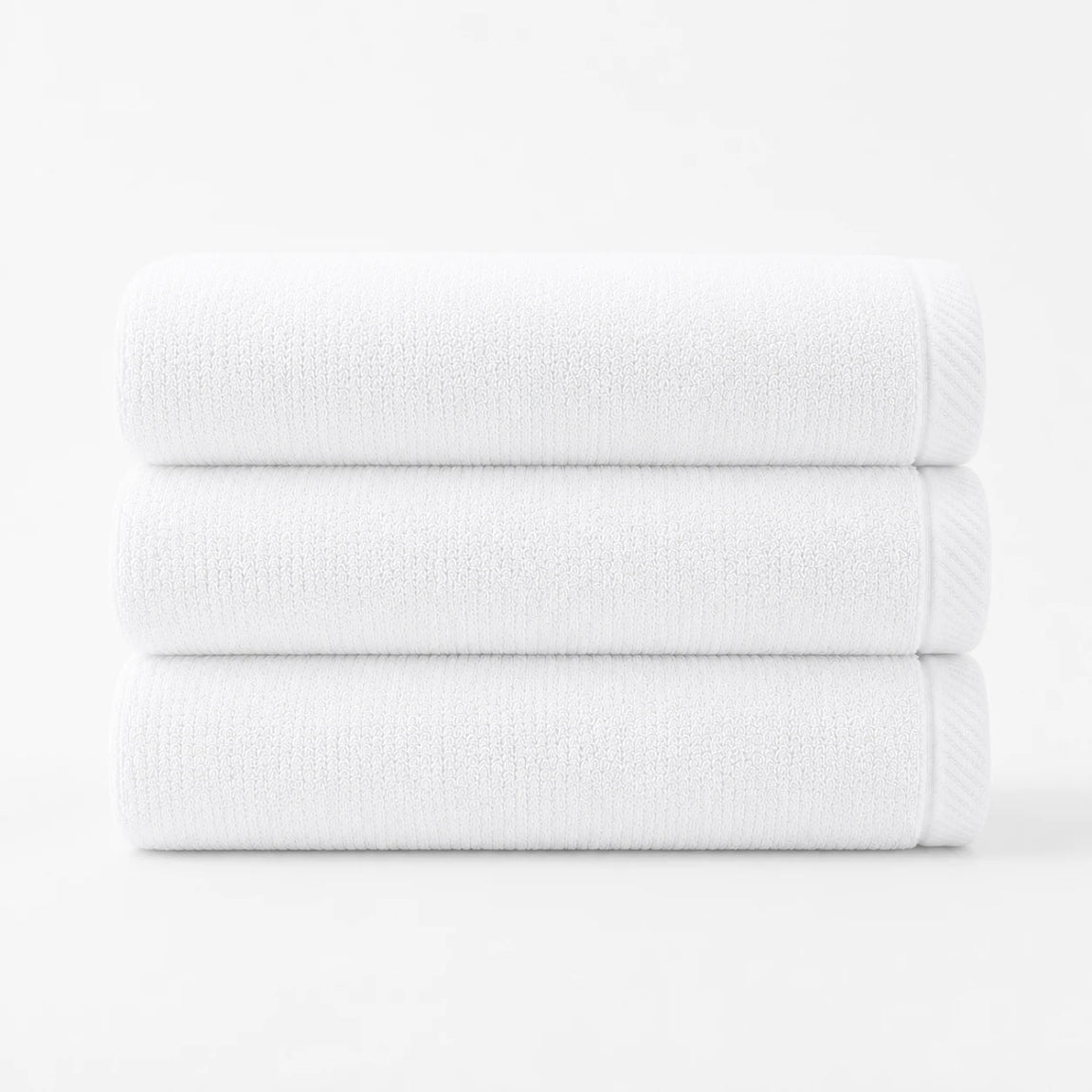 Three folded white cotton bath towels stacked together.
