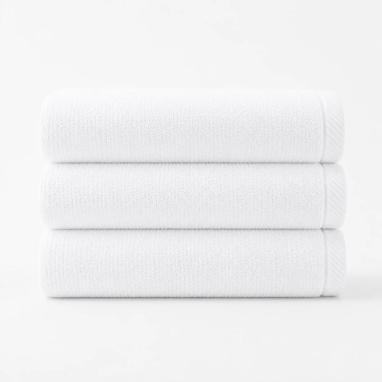 Three folded white cotton bath towels stacked together.