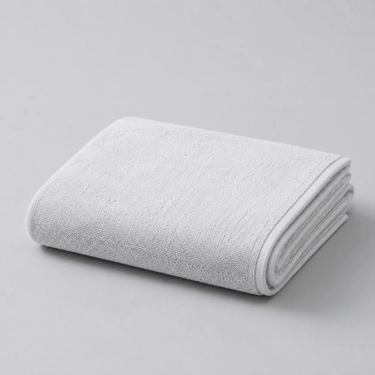 Folded white bath towel on a light grey surface.