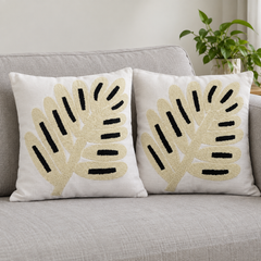 Two cream cushion covers with beige and black abstract leaf embroidery on a grey sofa.
