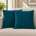 Two teal cushion covers with diagonal stitched lines on a cream sofa.