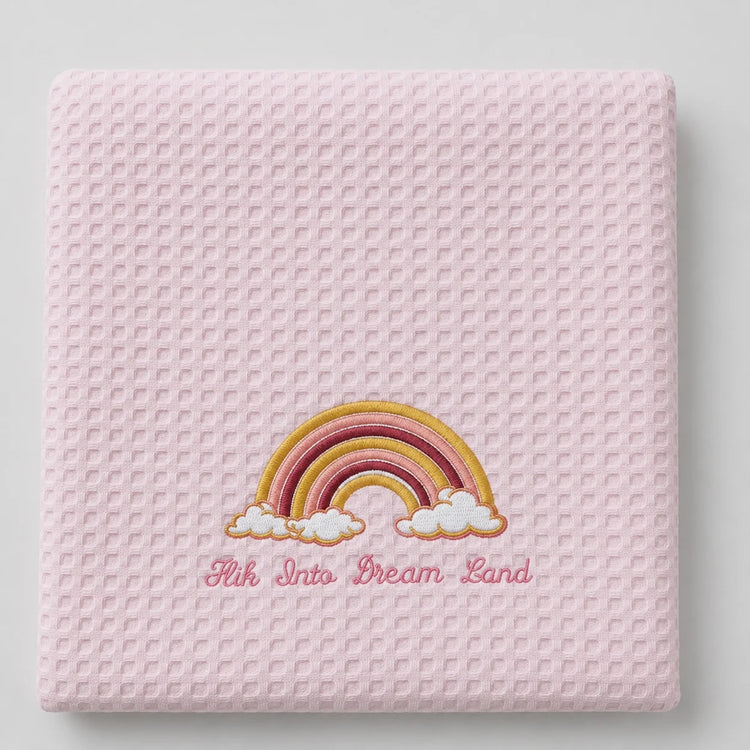 Folded pink waffle-weave baby blanket with a rainbow motif.