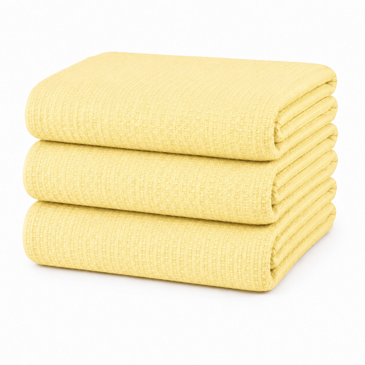 Stack of folded pale yellow waffle-textured blankets on a white background.