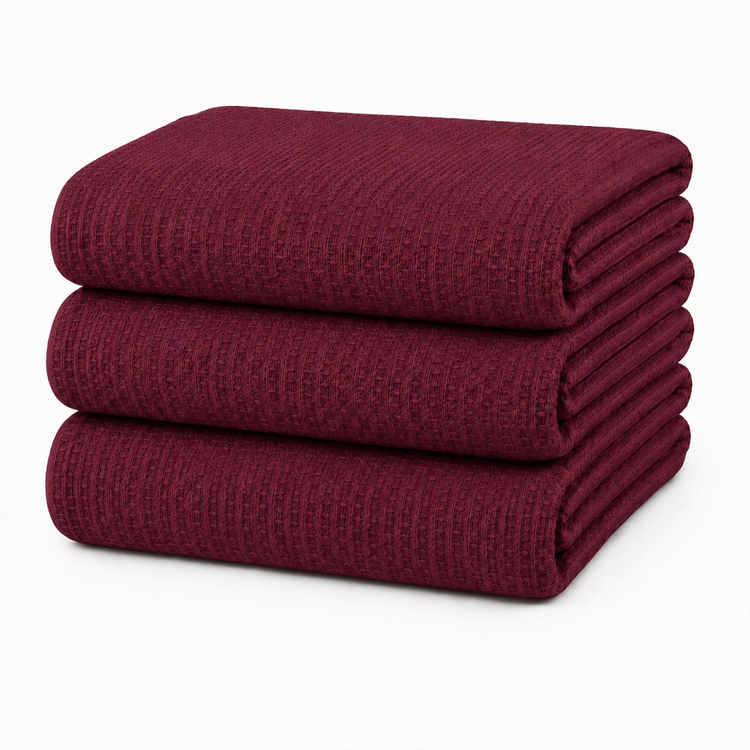 Stack of folded burgundy waffle-textured blankets on a white background.