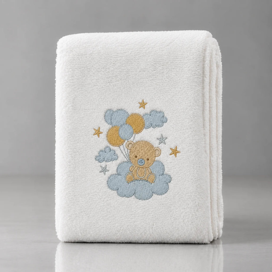 Folded white blanket with a teddy bear, blue and yellow balloons, clouds and stars