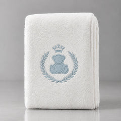 Folded white blanket with a crowned blue teddy bear inside a blue leafy wreath