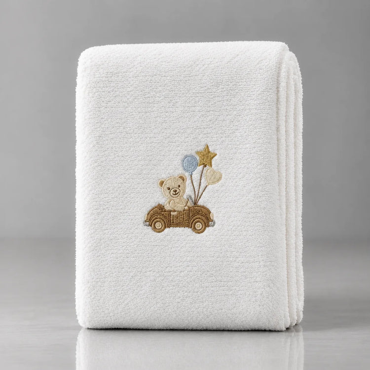 Folded white blanket with a teddy bear in a small car and balloons