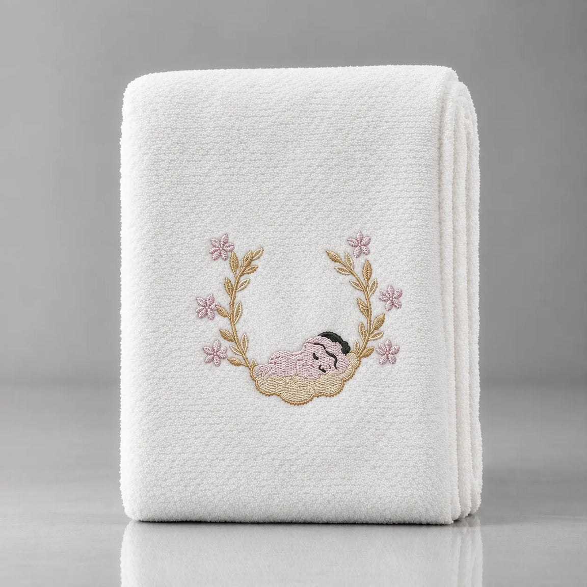 Folded white blanket with a sleeping baby motif framed by pink floral branches