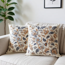 Two cream cushion covers with muted blue and brown floral patterns on a sofa.