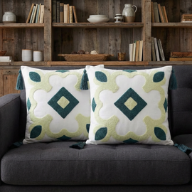 Two cream cushion covers with mint and dark green diamond motifs and tassels on a dark sofa.