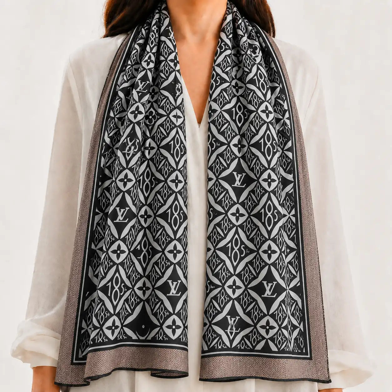 A black and white patterned scarf with Louis Vuitton monogram motifs, draped over the shoulders of a model wearing a white blouse.