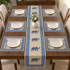 Alt Text: Wooden dining table set with white plates and cutlery, featuring a cream-colored table runner decorated with a repeating pattern of blue ornamental elephants and a blue floral border. with 6 mats
