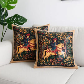 Two dark cushion covers with horses and riders surrounded by ornate floral borders on a sofa.