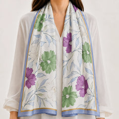 A lightweight white scarf with a colorful floral print in purple and green, styled around the neck of a model wearing a white blouse.