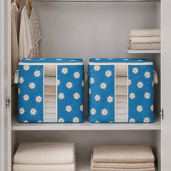 Two blue fabric storage bins with a white daisy pattern, filled with folded beige towels, displayed inside an open white closet on a shelf.