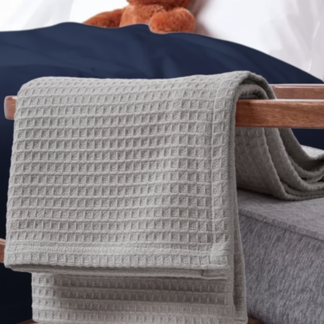 Ash gray waffle-textured blanket draped over a wooden chair arm beside a bed