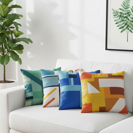 Four bright cushion covers with blue, green, yellow and orange colour-block designs on a sofa.