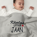 Infant under a gray waffle-textured blanket with Khalas Little Jaan lettering and a red heart