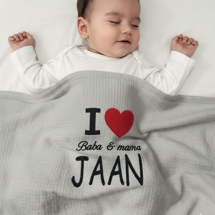 Infant under a gray waffle-textured blanket with a red heart and Baba & mama Jaan lettering