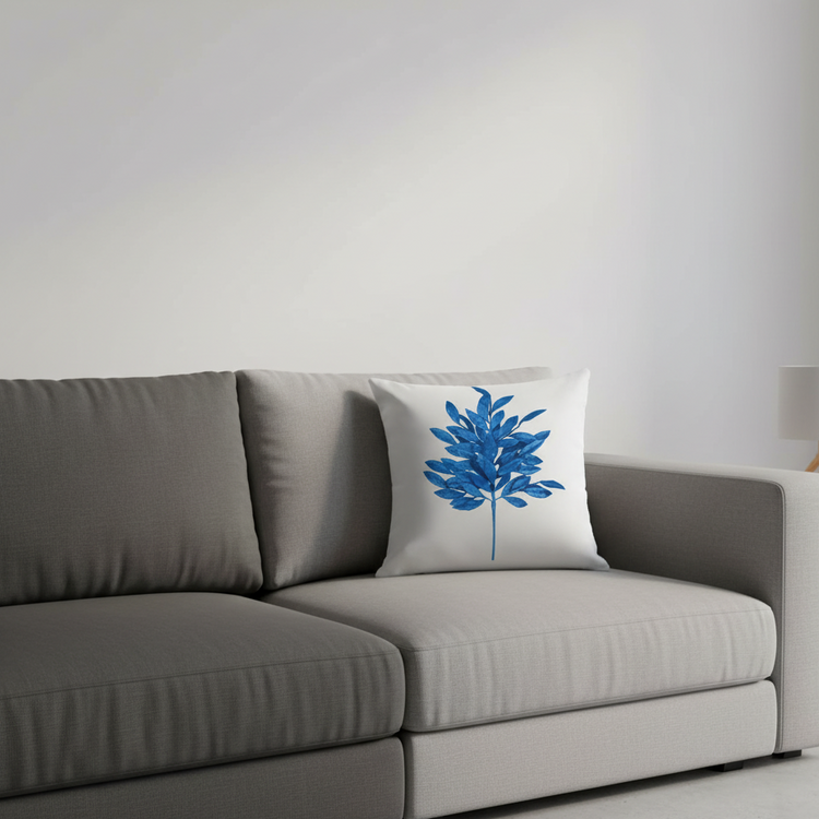 White cushion cover with a blue leafy branch displayed on a grey sofa.