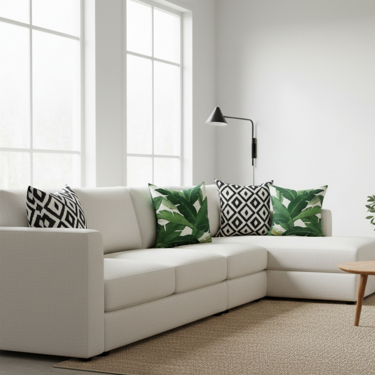 Green leaf and black and white geometric cushion covers arranged on a corner sofa.