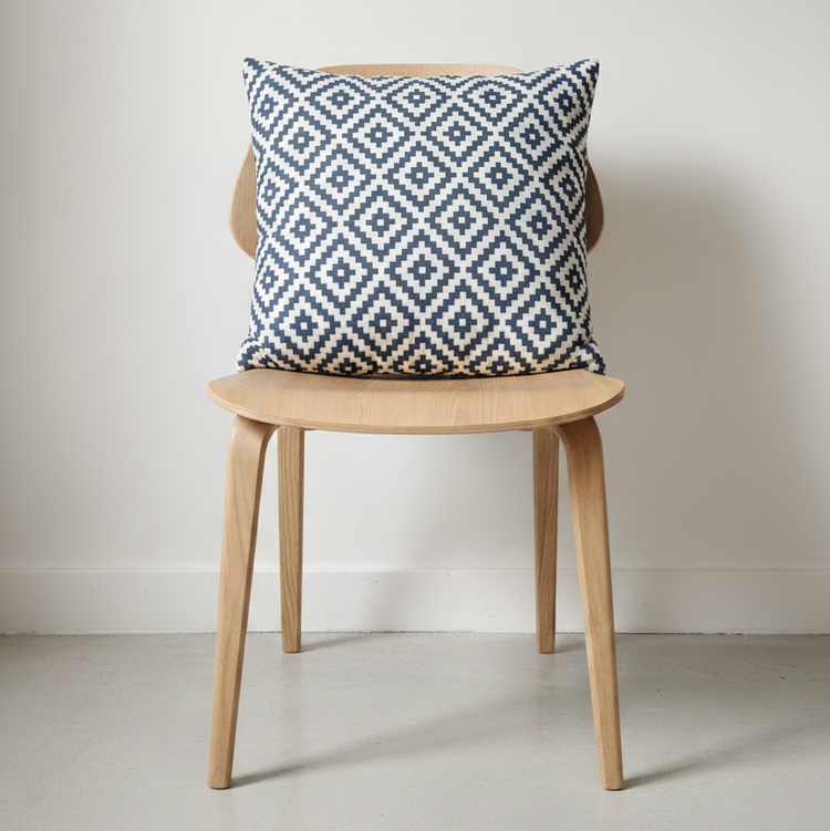 White cushion with repeating blue-grey diamonds displayed on a wooden chair.