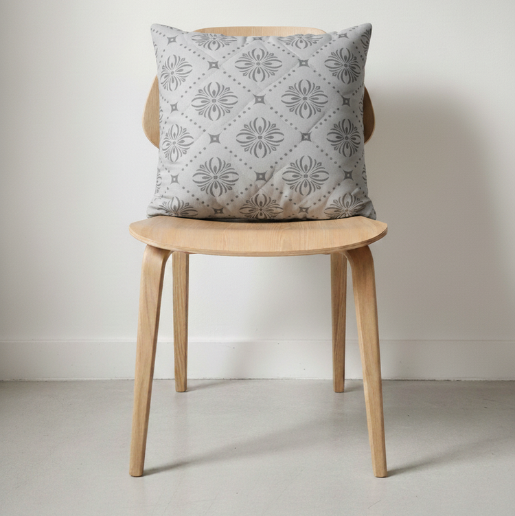 Pale grey cushion with delicate circular floral motifs displayed on a wooden chair.