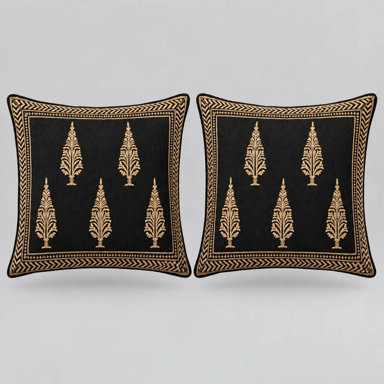 Two square black throw pillows with gold embroidered tree motifs and a decorative gold border, shown side by side on a light gray background.