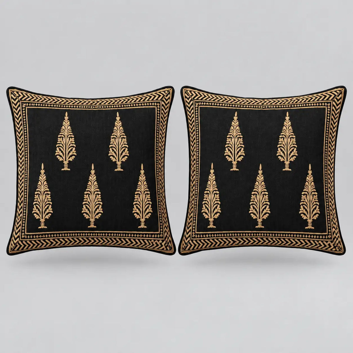 Two square black throw pillows with gold embroidered tree motifs and a decorative gold border, shown side by side on a light gray background.