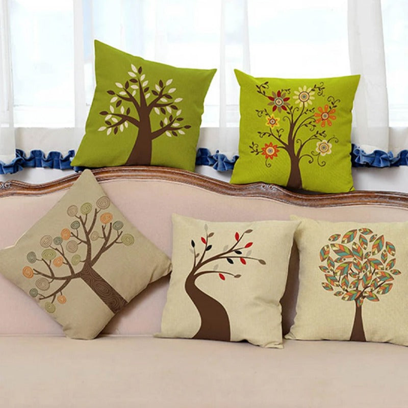 Five green and cream cushion covers with different tree designs on a sofa.
