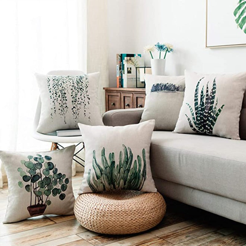 Green botanical cushion covers displayed on a sofa, chair and woven stool.